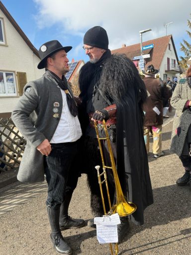 Zwei Männer in historischen Kostümen stehen in einem Dorf auf der Straße.
