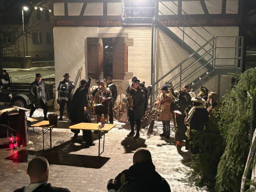 Gruppe von Menschen bei einer nächtlichen Veranstaltung im Freien, umgeben von Gebäuden.