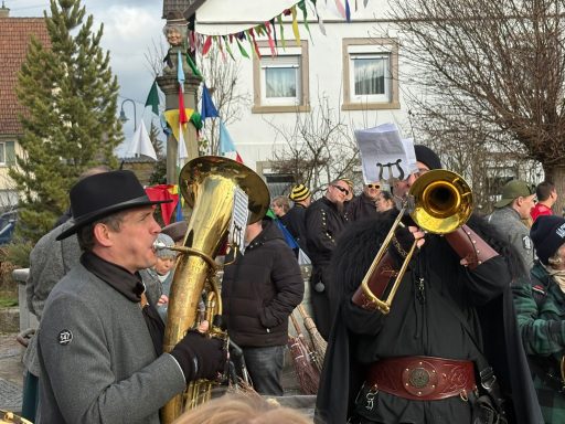 Zwei Musiker spielen Blasinstrumente vor einer Menge in einem festlichen Ambiente.