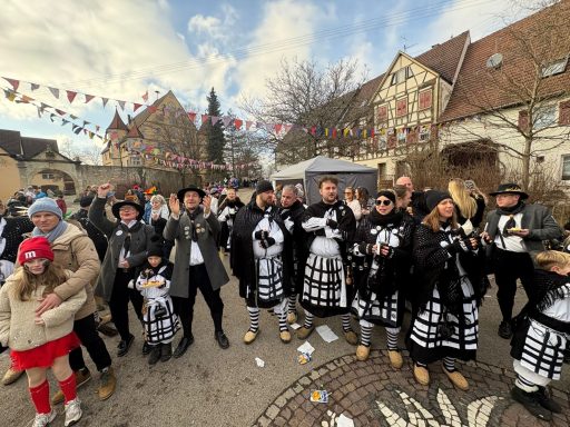 Menschen in traditionellen Kostümen feiern zusammen auf einer Straßenfest, umgeben von bunten Fähnchen.