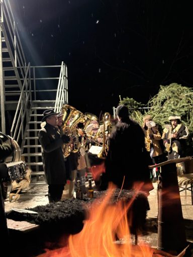 Musiker spielen im Dunkeln neben einem Feuer, umgeben von Bäumen und einer Treppe.