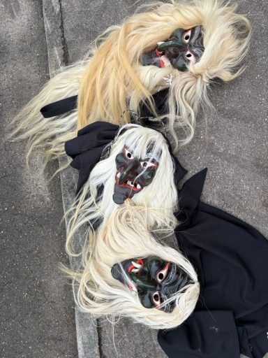 Drei maskierte Köpfe mit langen, blonden Haaren auf dem Boden liegend.