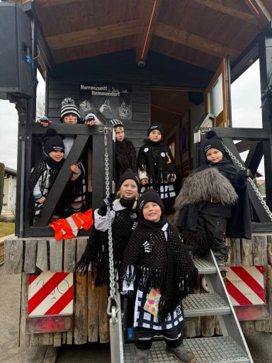 Gruppe von Kindern in schwarz-weißen Kostümen vor einem Veranstaltungswagen.