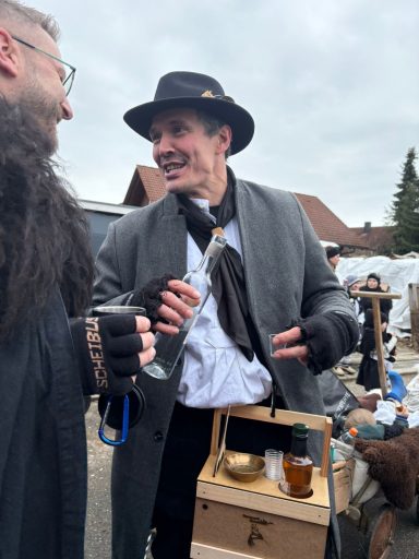 Mann in einem Hut lächelt und hält eine Flasche, umgeben von einer festlichen Atmosphäre.