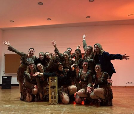 Gruppe von Tänzerinnen in festlichen Kostümen, fröhliche Pose mit Händen in der Luft.