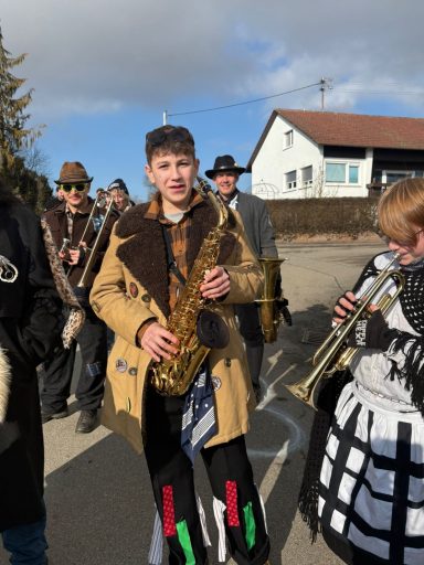 Jugendliche in festlicher Kleidung spielen Blasinstrumente auf einer Straße.