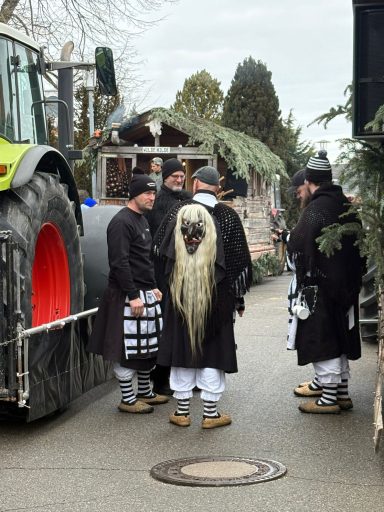 Fünf Personen in traditionellen Kostümen mit langen Haaren stehen an einer Straße.