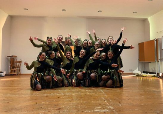 Gruppe von Tänzerinnen in grünen Kostümen, die fröhlich posieren.