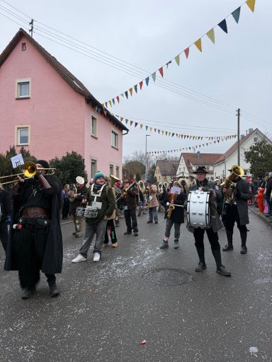 Karnevalsumzug mit Trompetenbläsern und bunten Fahnen in einer festlich geschmückten Straße.