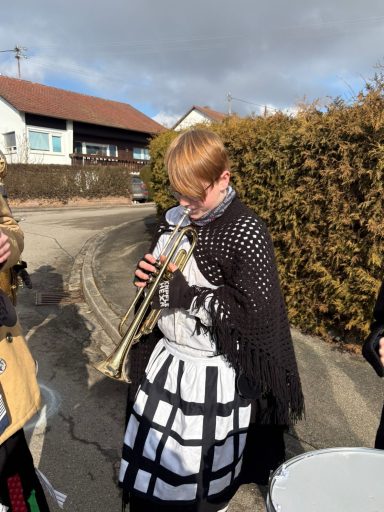 Eine Person in schwarzer Kleidung spielt Trompete auf einer Straße.
