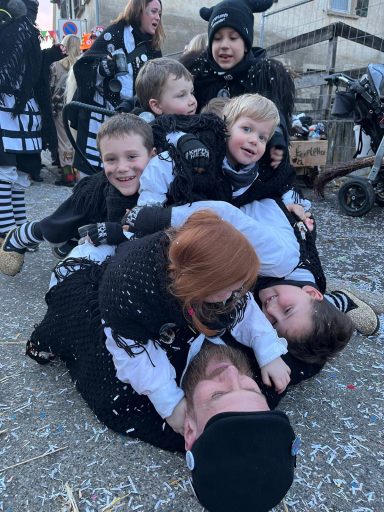 Gruppenspiel mit Kindern und Erwachsenen in Kostümen, auf einem Kunstrasen liegend.