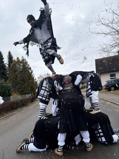 Tanzende Gruppe in traditioneller Kleidung bildet einen menschlichen Turm auf einer Straße.