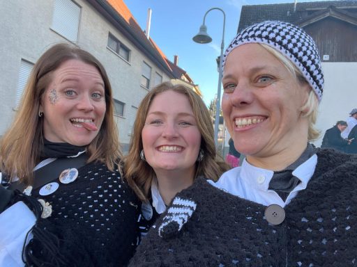 Drei Frauen in schwarzen Schals lächeln fröhlich und posieren für ein Foto.