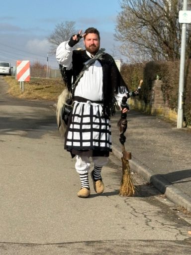 Mann in traditioneller Kleidung mit Besen auf einer Straße.