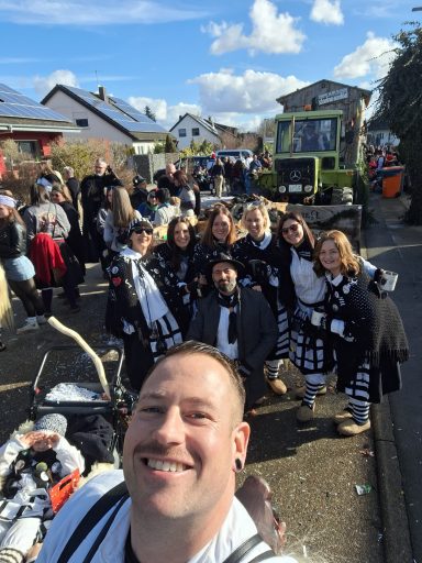 Mann im Vordergrund mit Gruppe von Menschen in Kostümen auf einer festlichen Straße.