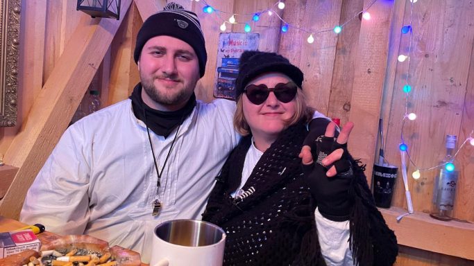 Ein Mann und eine Frau in winterlicher Kleidung sitzen zusammen in einem festlich dekorierten Raum.